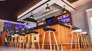 A bar area with wooden stools, a counter with bottles, and pendant lighting. - Romeos Hotel (Kampala)