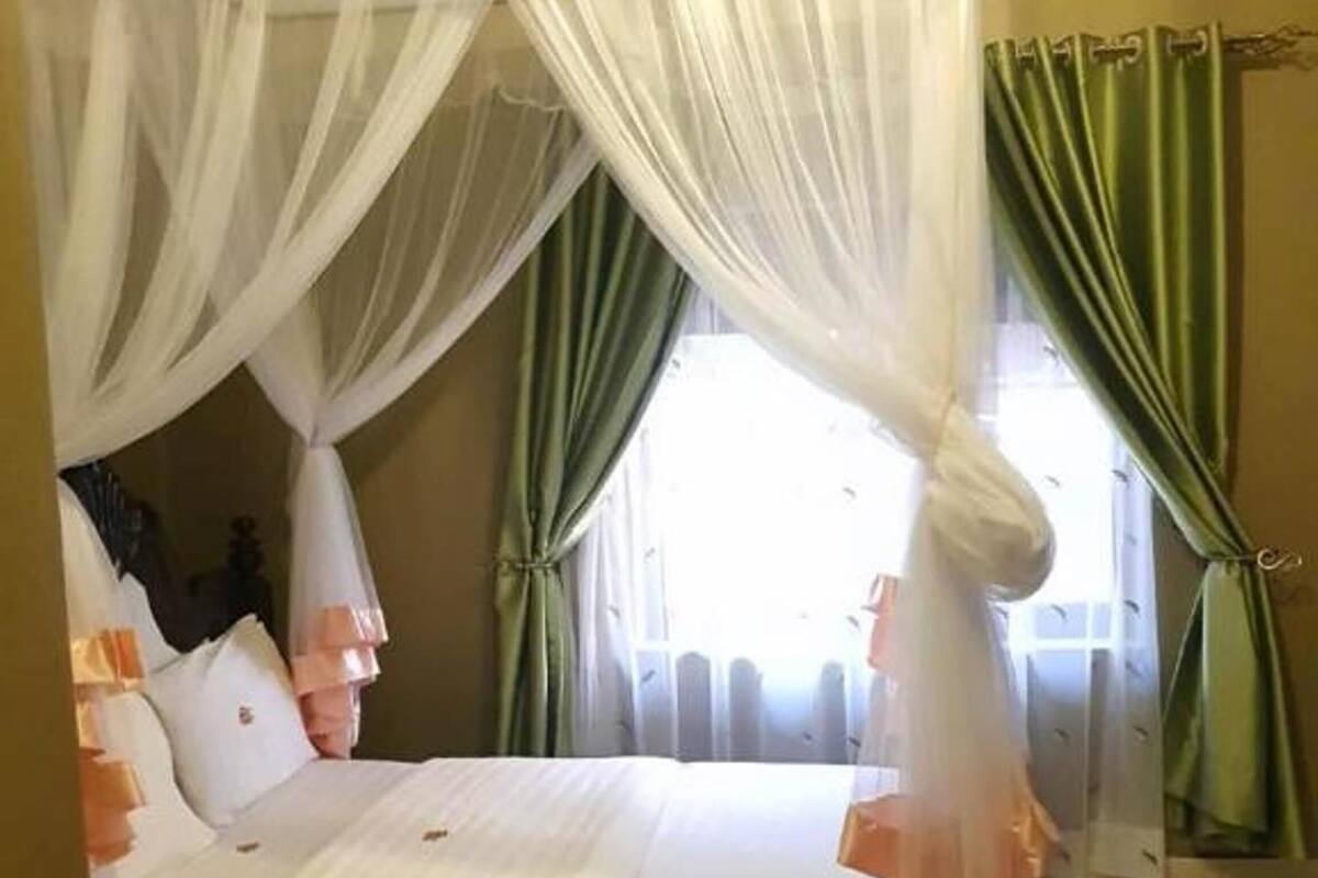 A bed with a canopy, green curtains, and a view of the outdoors.