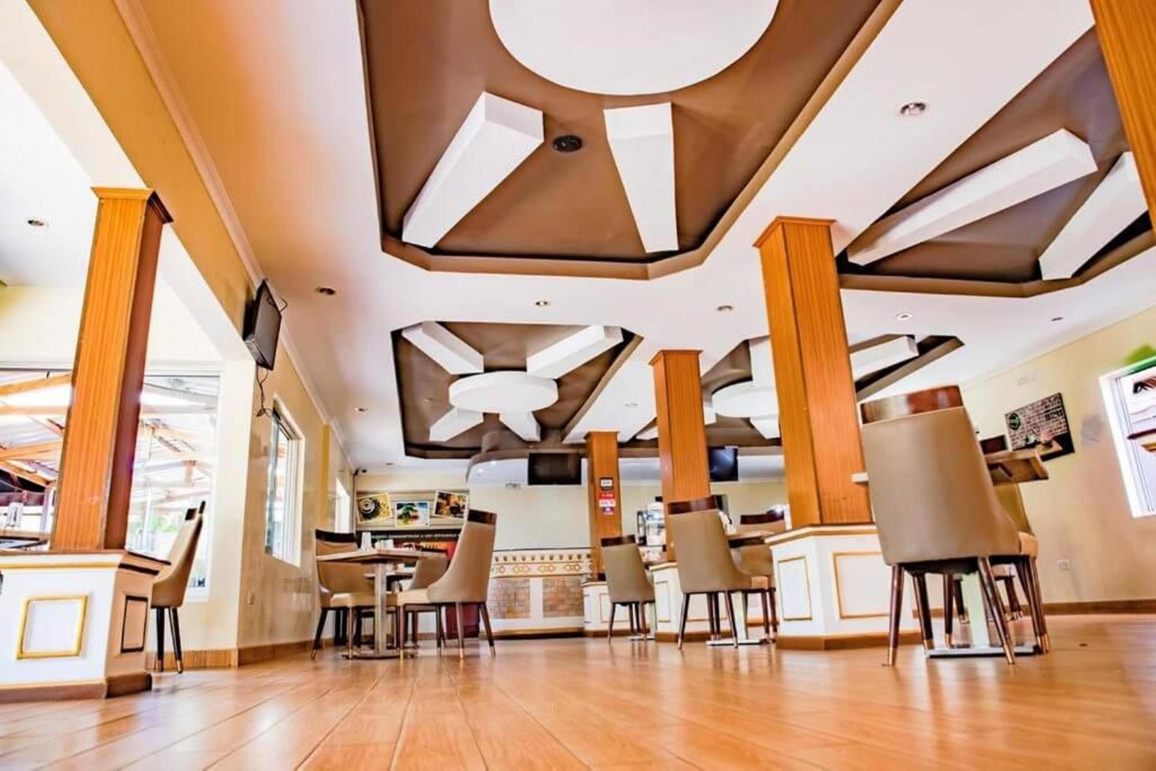 Een ruim restaurant met hoge plafonds, houten zuilen en een centrale plafondventilator.