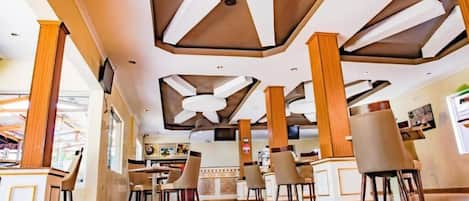 Un restaurante espacioso con techos altos, pilares de madera y un ventilador de techo central.