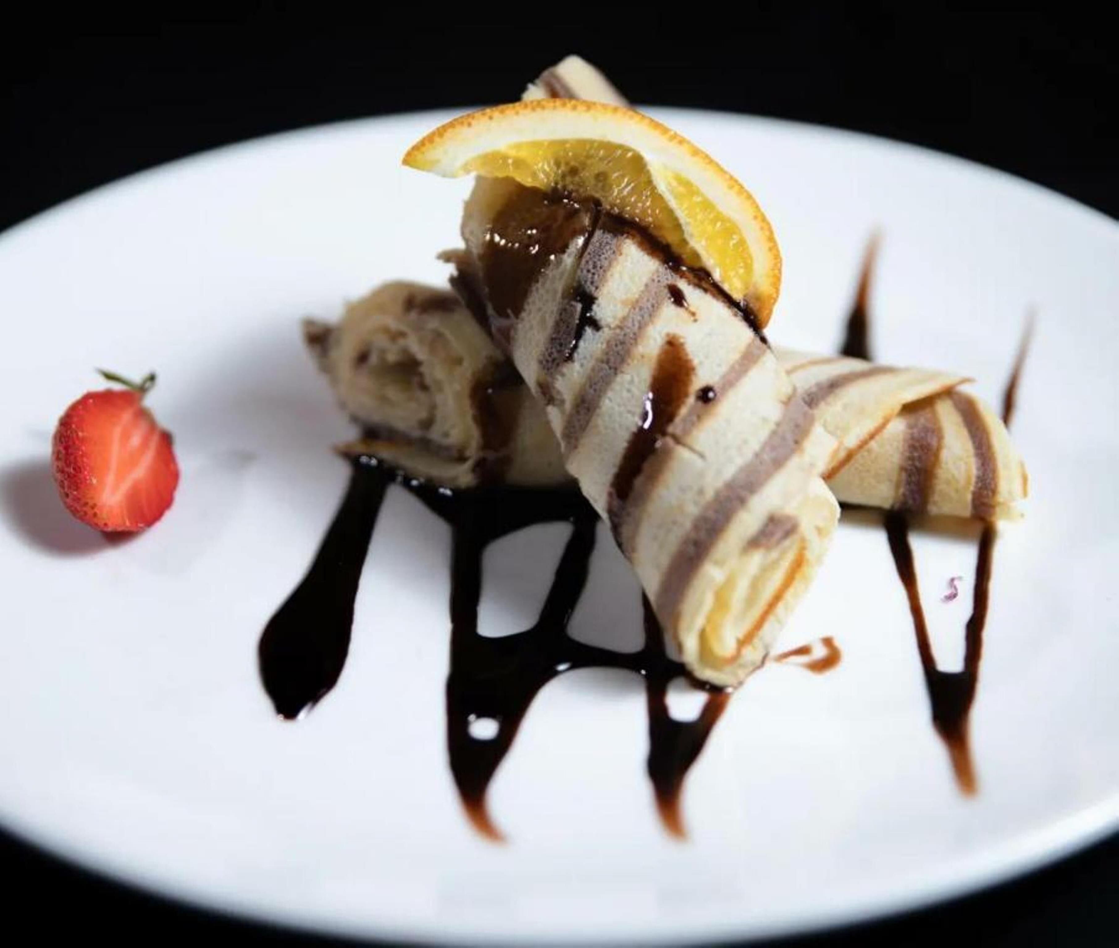 A dessert plate with rolled crepes, a strawberry, and chocolate sauce.