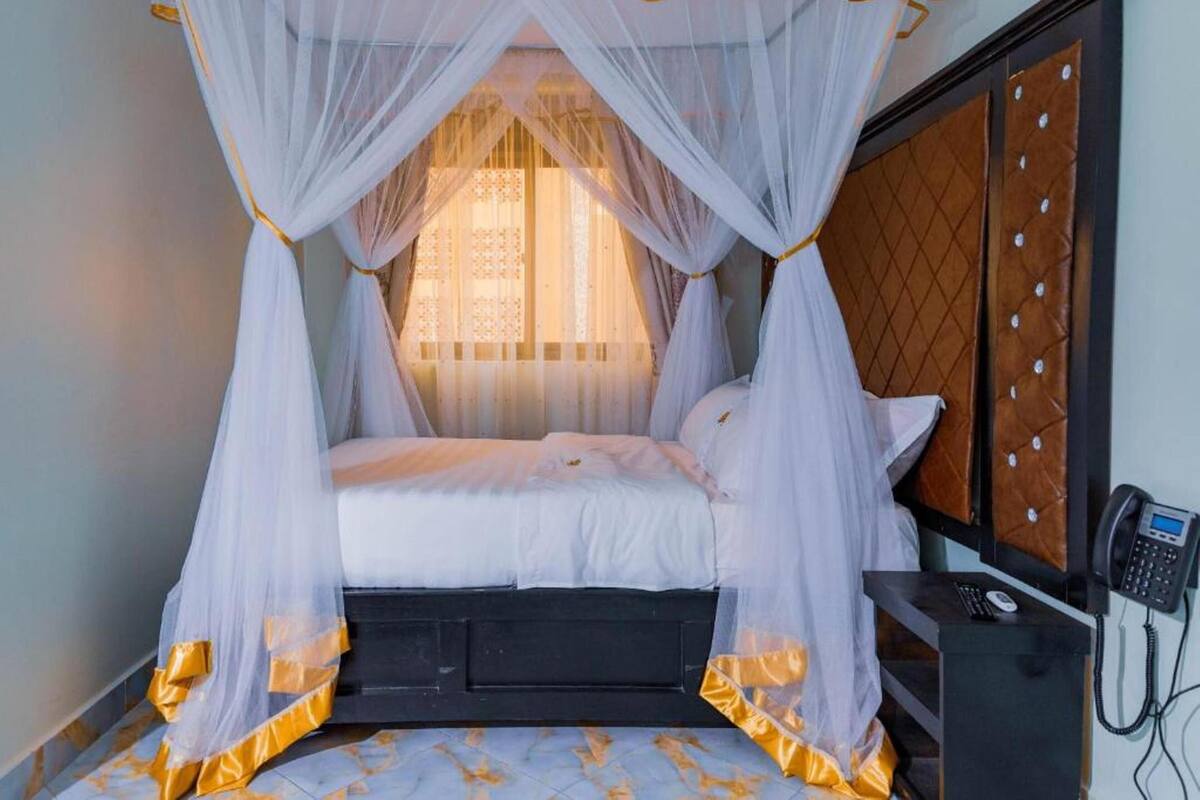 A bed with a canopy, a bedside phone, and a patterned wall.