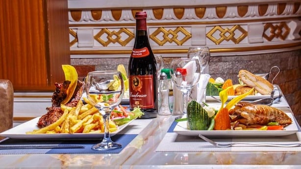 A dining table set with a bottle of wine, a glass, and plates of food including fries, salad, and grilled meat. - Romeos Hotel (Kampala)