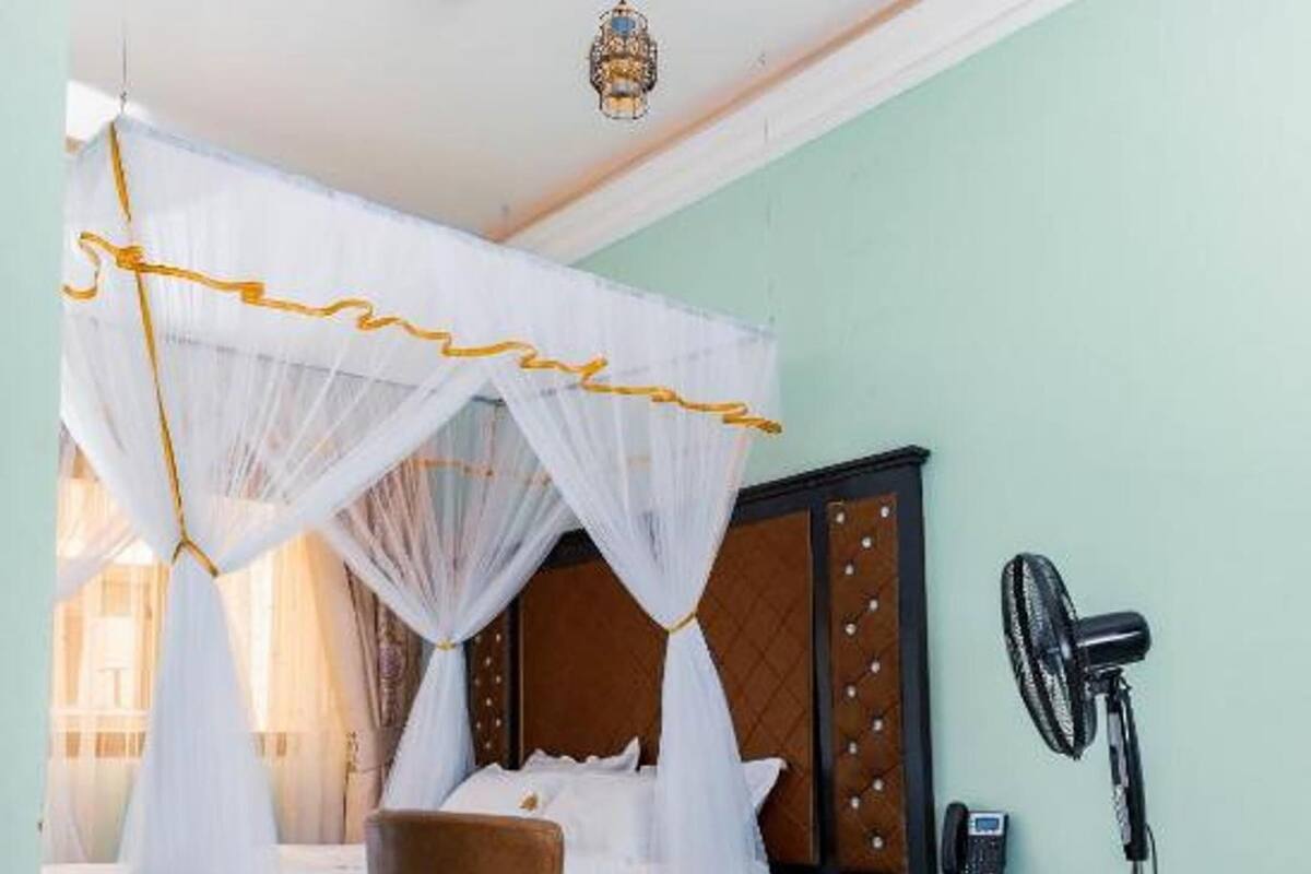 A hotel room with a bed, a chair, a small table, a fan, and a telephone.