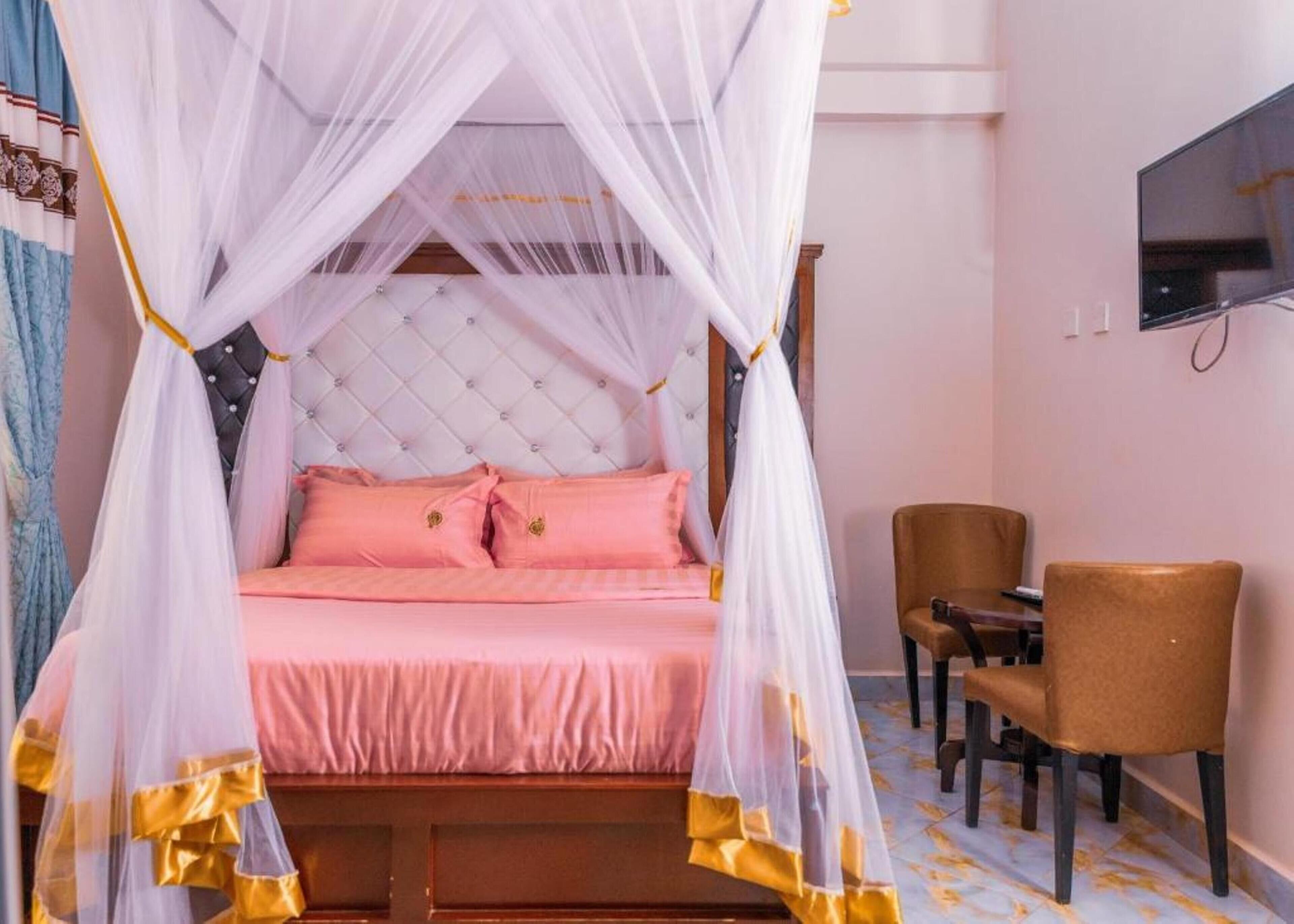 Un dormitorio con cama bajo dosel, televisor en la pared y dos sillones.
