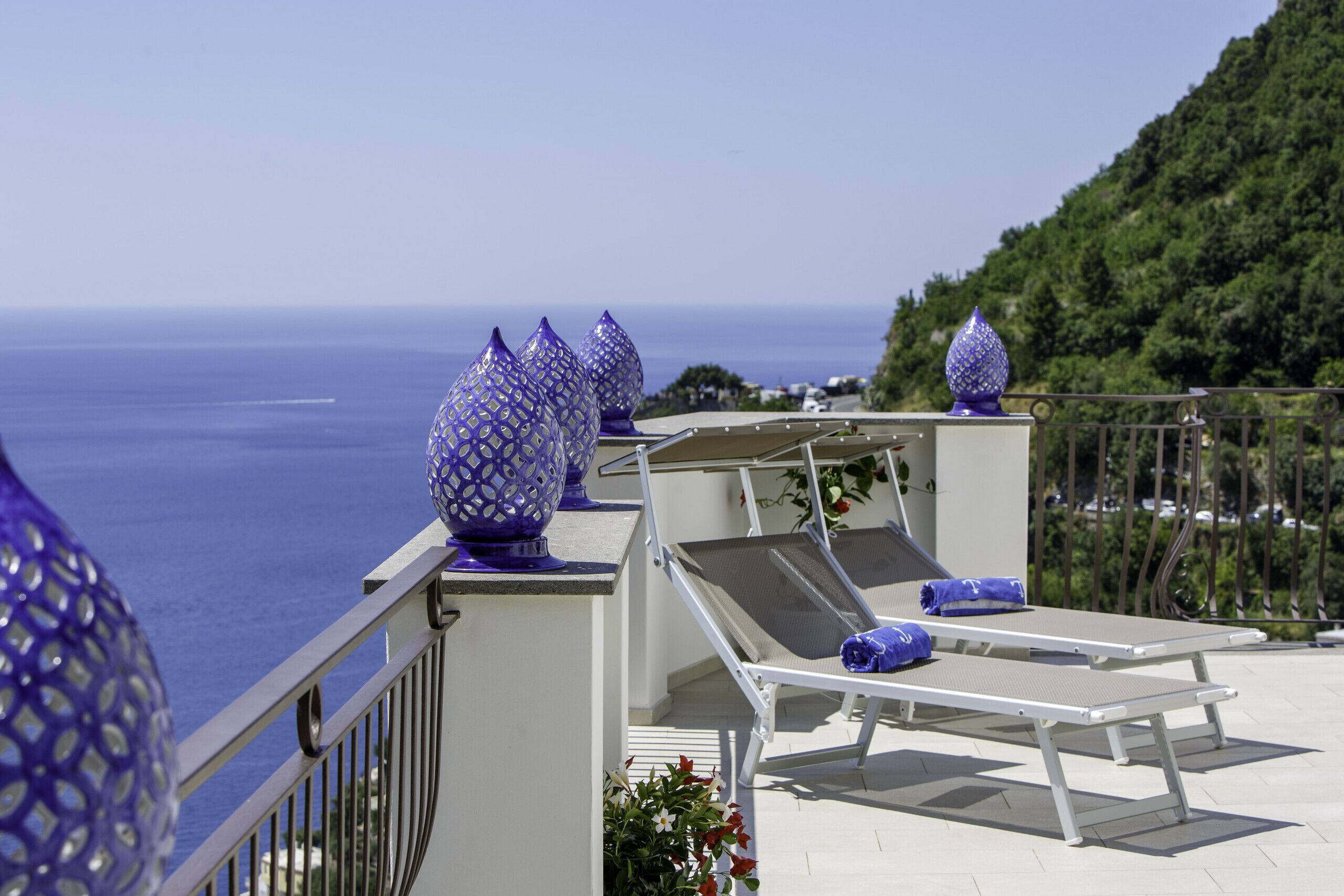 Un balcon avec vue sur la mer, des chaises longues et des vases décoratifs bleus.