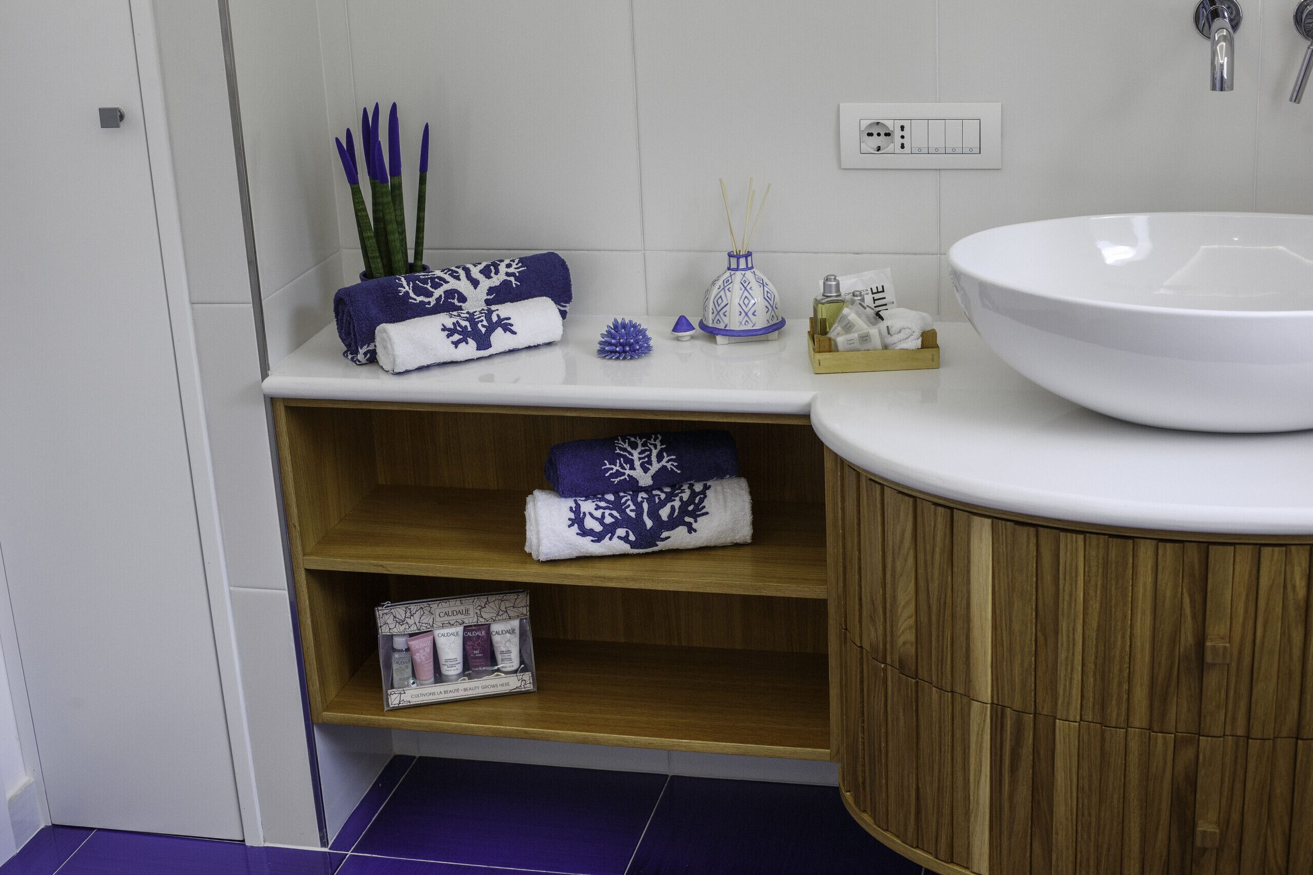 A bathroom with a white sink, wooden shelves, and a purple tiled floor.