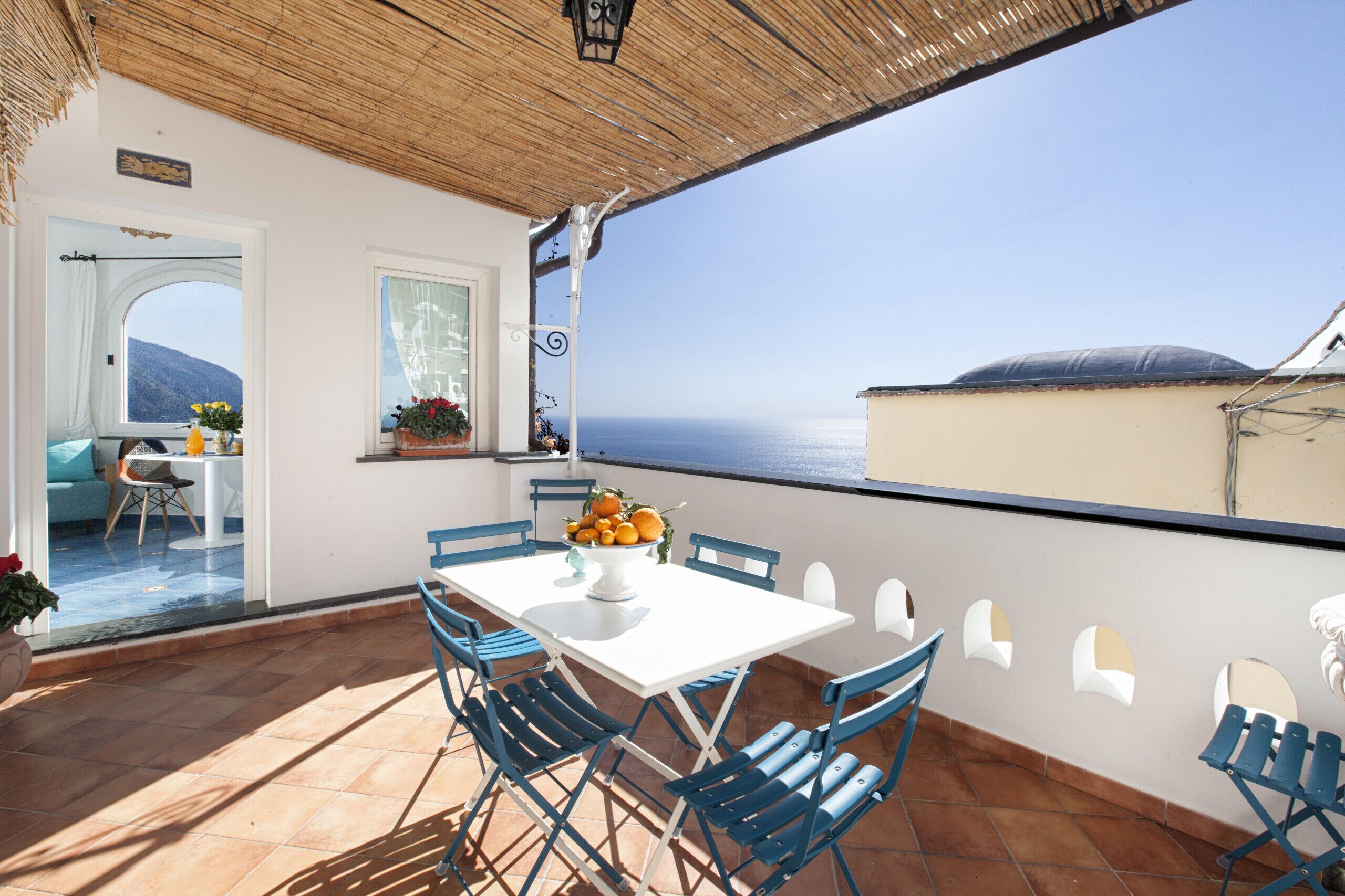 Una terraza con una mesa blanca y sillas azules, con vista al mar.