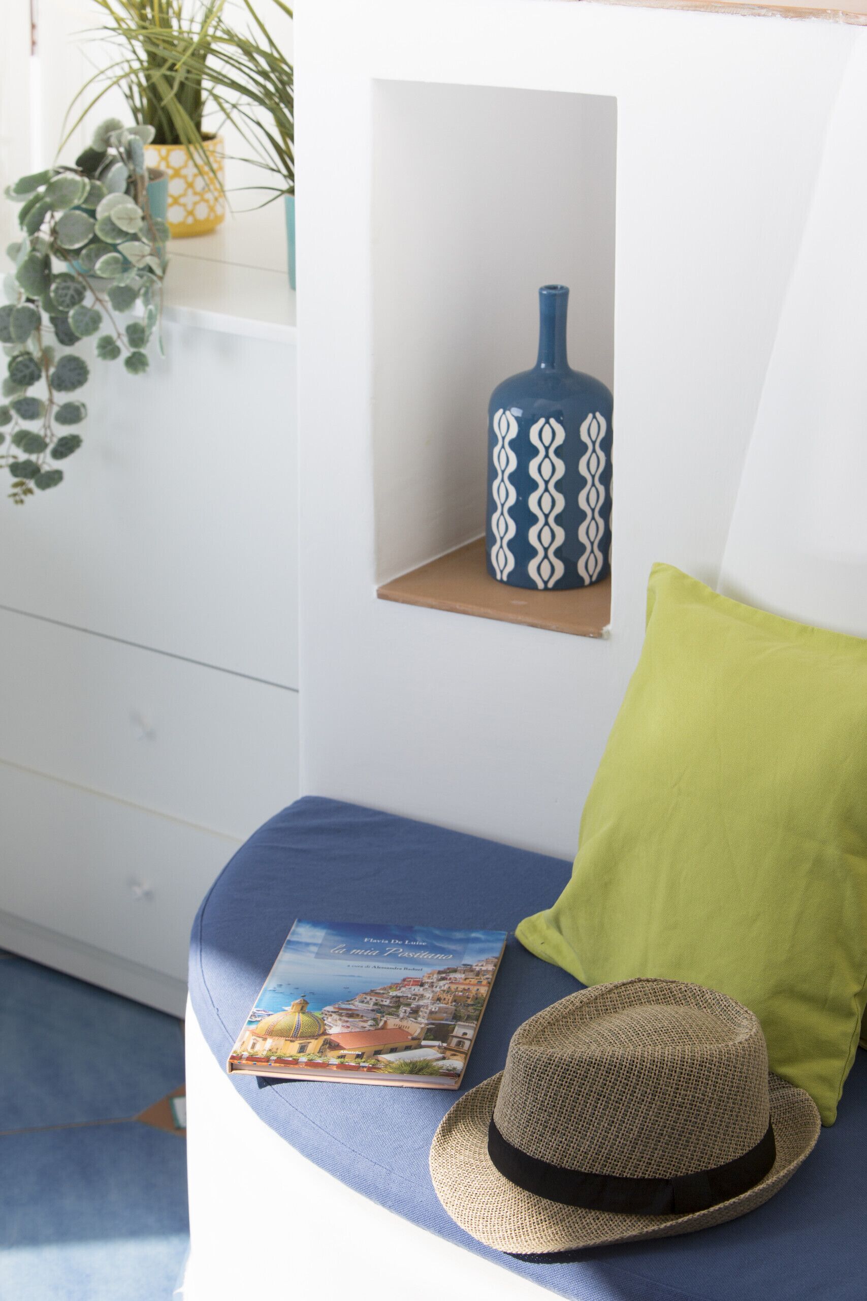 A room with a blue sofa, a green pillow, a hat, and a book on the sofa.
