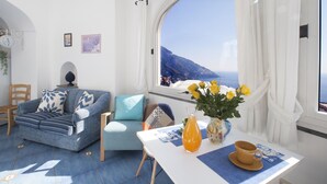 A bright room with a large window, a sofa, a table with a vase and a cup, and a chair. - Villa Settemari (Positano)