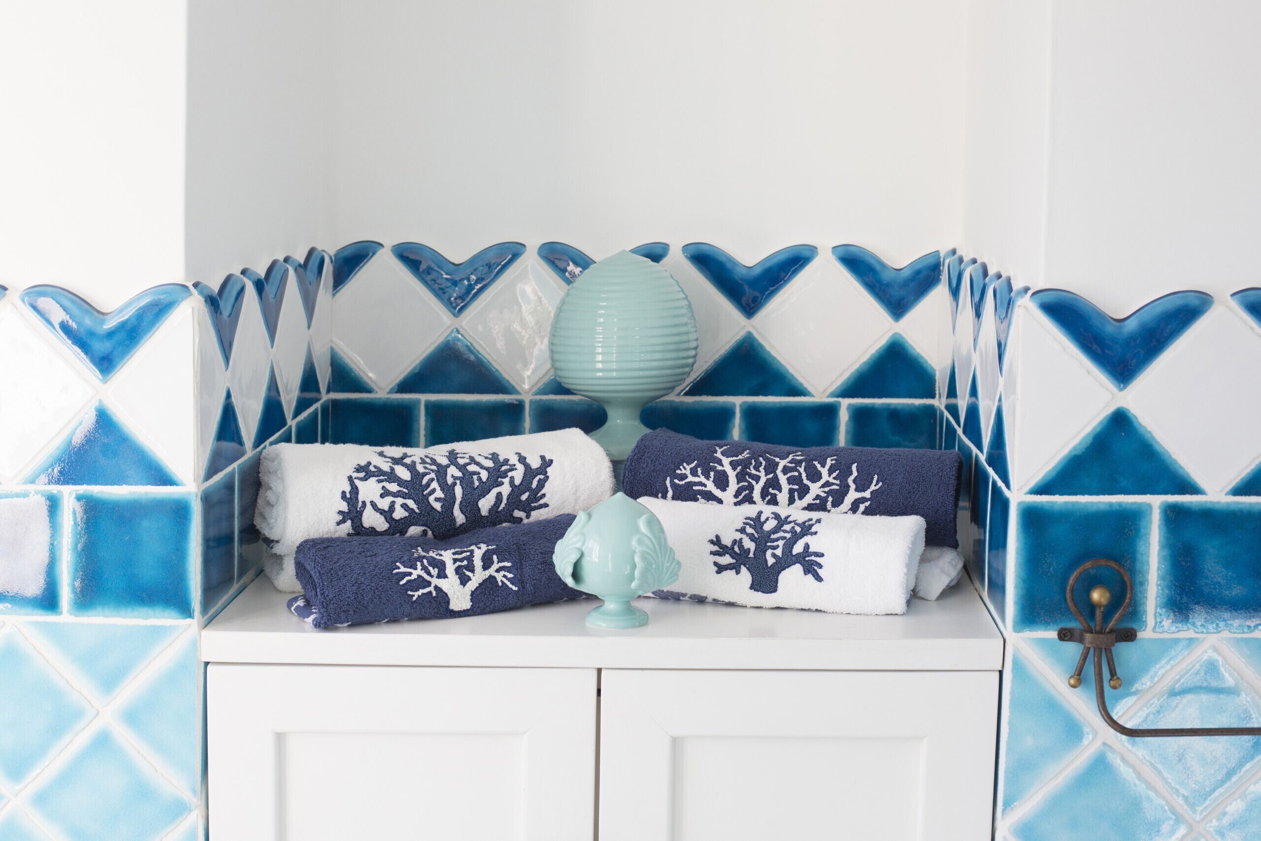 A bathroom with a white vanity, a blue and white tiled wall, and towels with tree patterns.