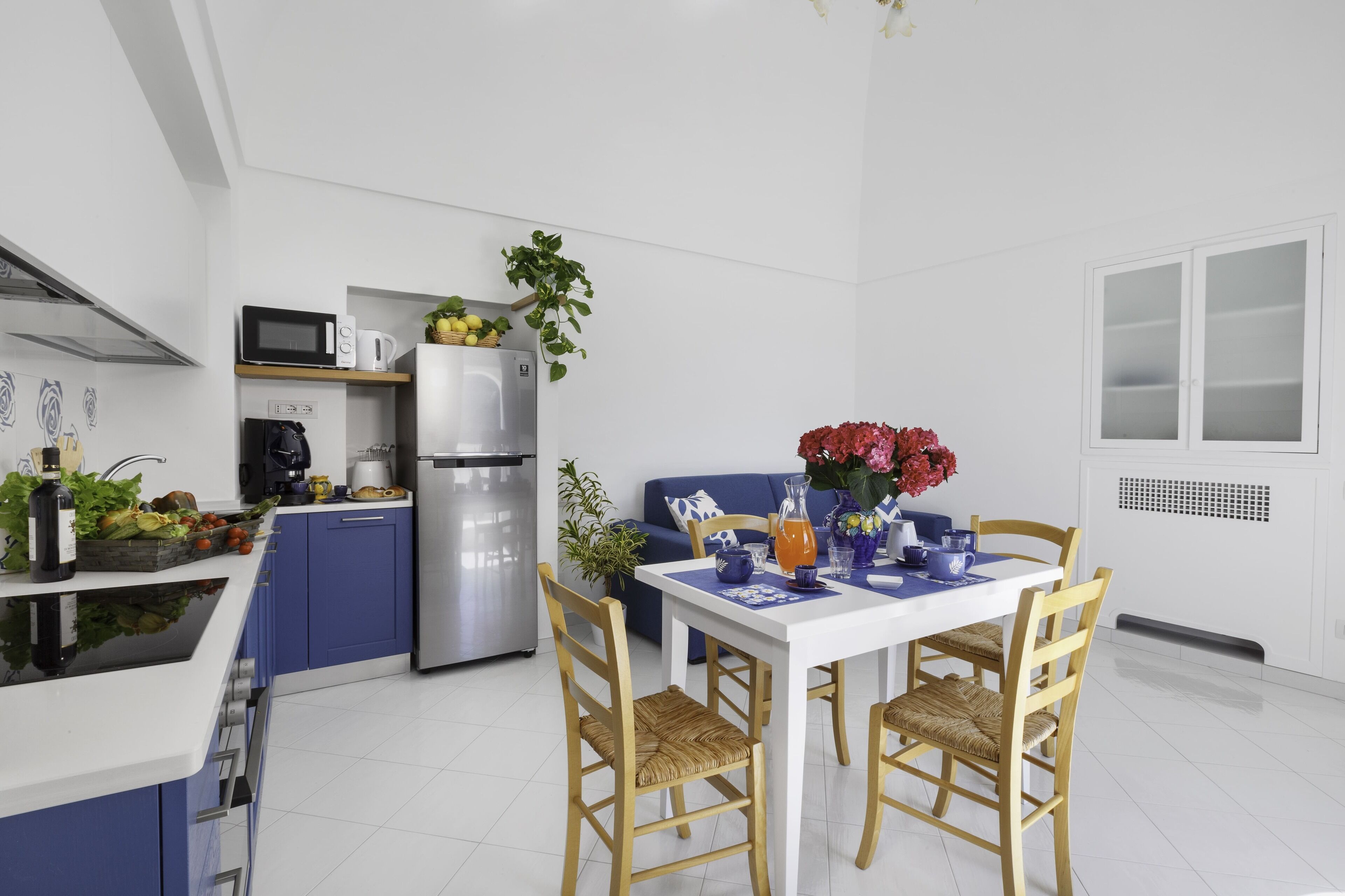 Eine moderne Küche mit weißer Arbeitsplatte, blauen Schränken und einem Essbereich mit weißem Tisch und Holzstühlen.