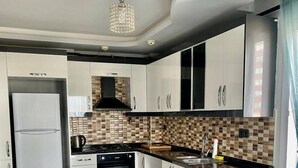 A modern kitchen with white cabinets, a black stove, and a tiled backsplash. - Palmiye Gold (Mersin)