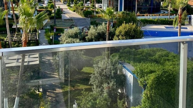 A high-rise residential building with multiple balconies, surrounded by palm trees and a swimming pool. - Palmiye Gold (Mersin)