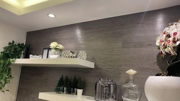 Un interior moderno con paneles de madera, estanterías blancas que exhiben objetos decorativos y una planta en maceta.