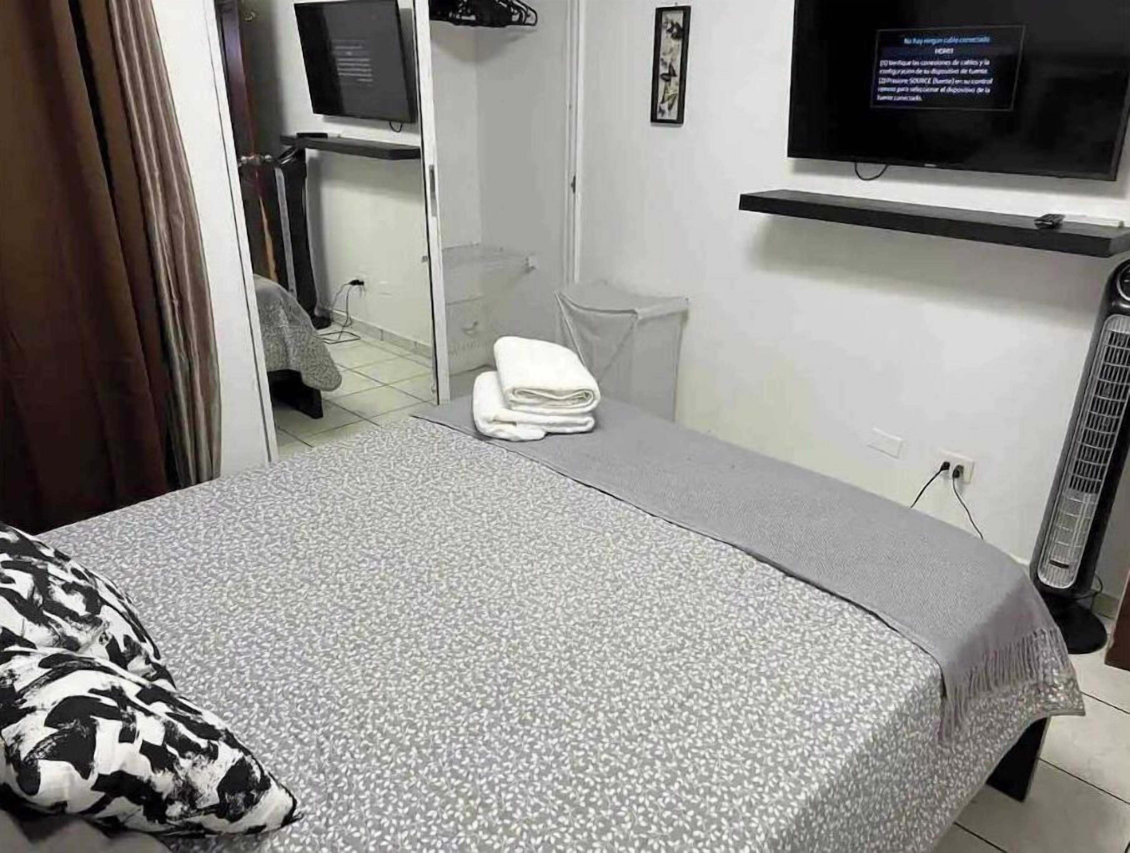 Una habitación de hotel con una cama, televisor montado en la pared, una mesita y una silla.
