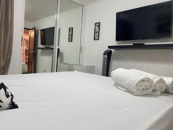 A hotel room with a bed, a flat-screen TV mounted on the wall, a mirror, and a rolled towel on the bed. - ,self check-in,beautiful, céntric, first floor. (Santiago De Los Caballeros)