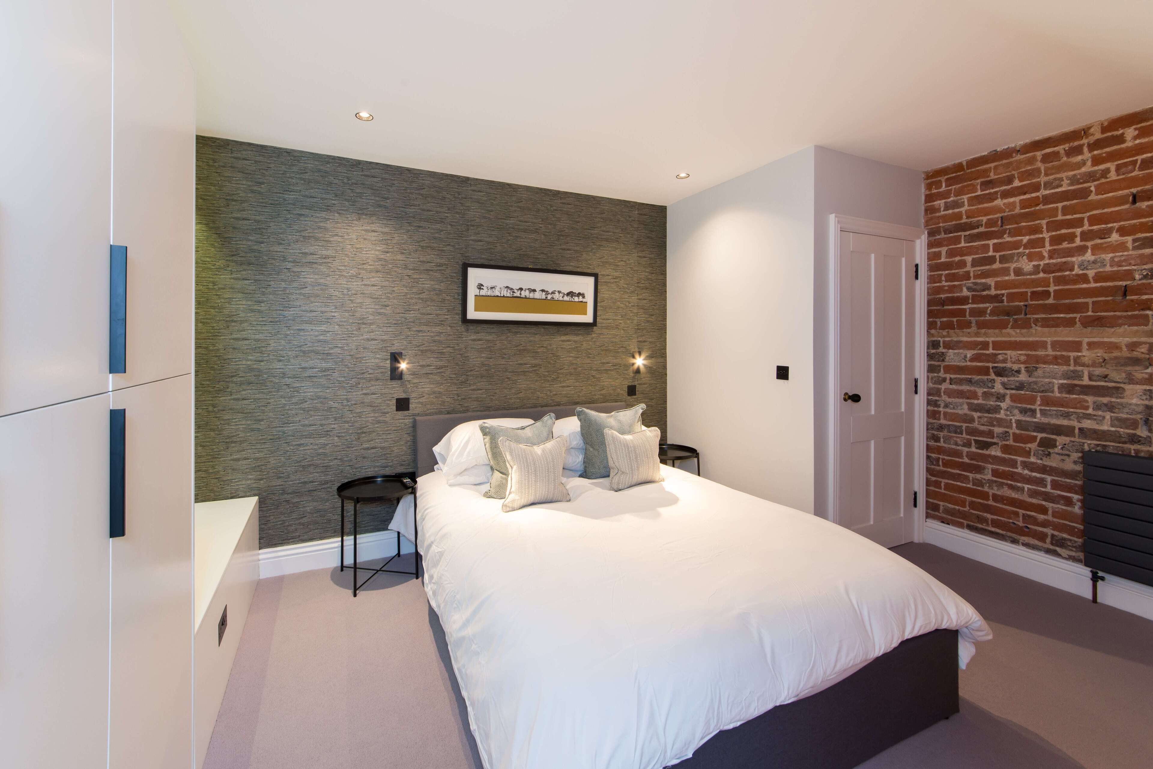 A modern bedroom with a large bed, a brick wall, and a framed picture on the wall.