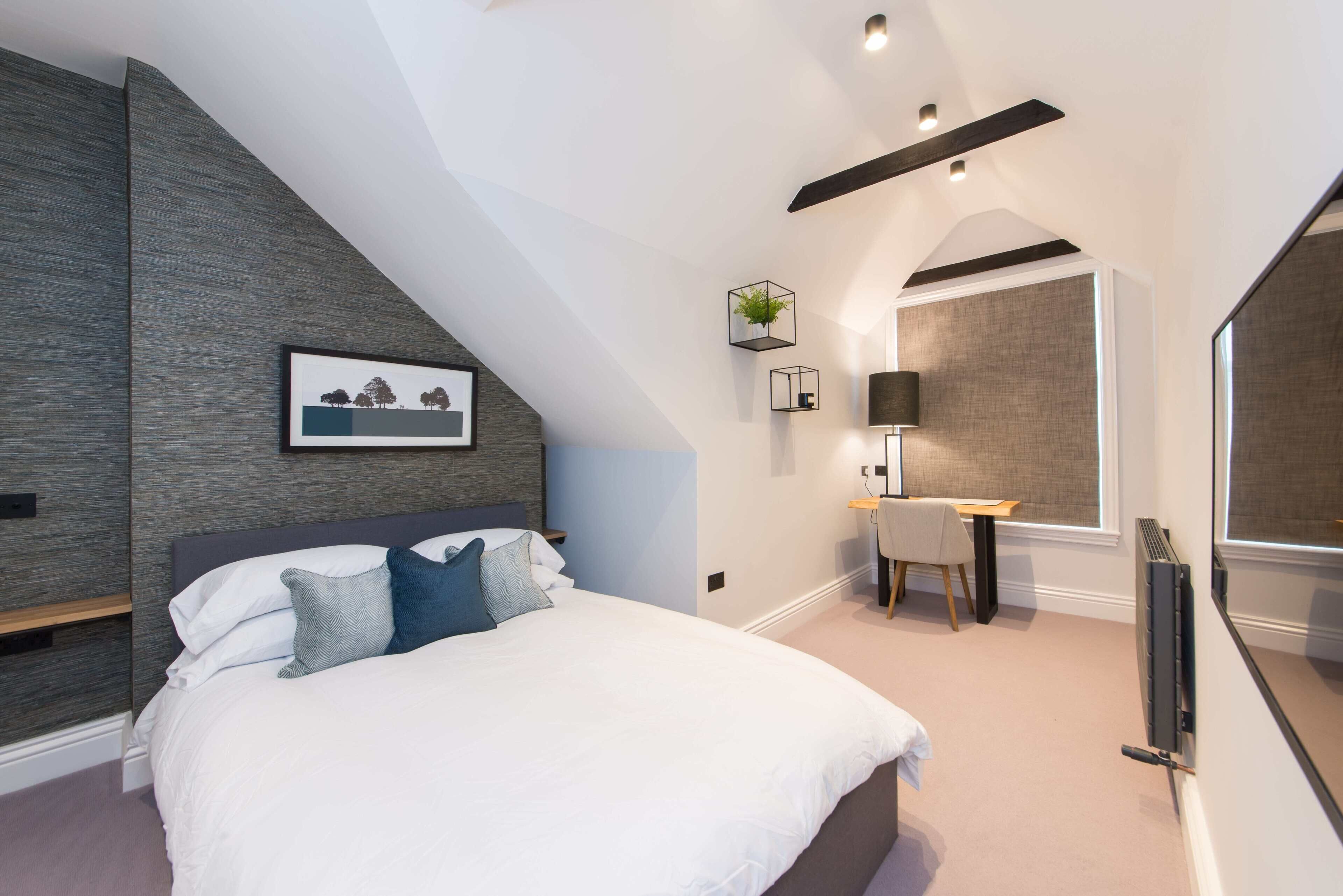 A bedroom with a bed, bedside table, lamp, and a framed picture on the wall.