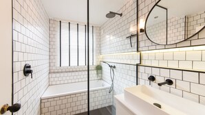 Et moderne badeværelse med hvide, rektangulære fliser, en glas brusekabine, et badekar og en hvid vask.