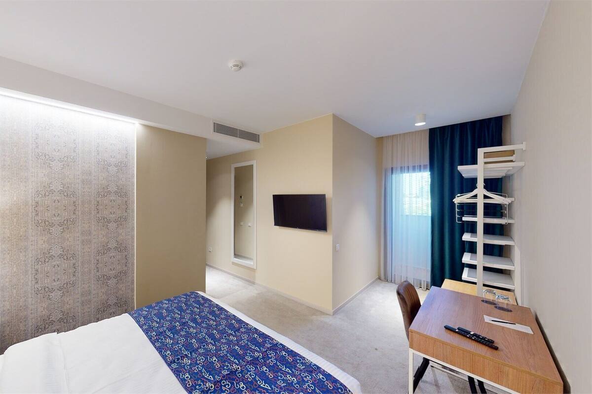 A hotel room with a bed, a desk, a chair, a TV, and a wardrobe.