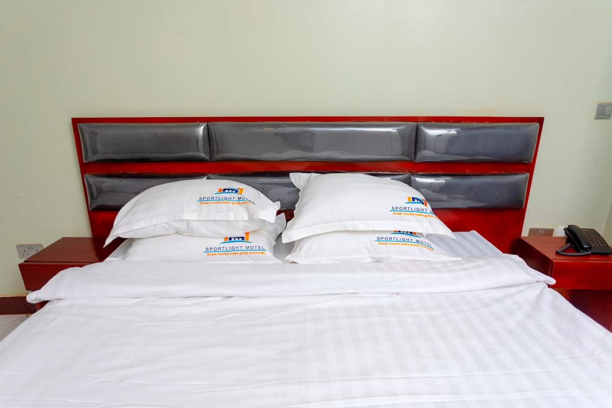 A neatly made bed with white linens and pillows, a red headboard, and a bedside table with a phone.