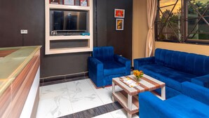 A room with a dark wall, a large window with curtains, a blue sofa, a blue armchair, and a small table with a vase of flowers. - Spotlight Motel (Kampala)
