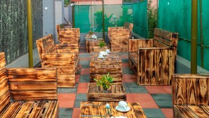 A patio area with wooden furniture arranged in a semi-circle, a small table with a plant, and a TV mounted on the wall. - Spotlight Motel (Kampala)
