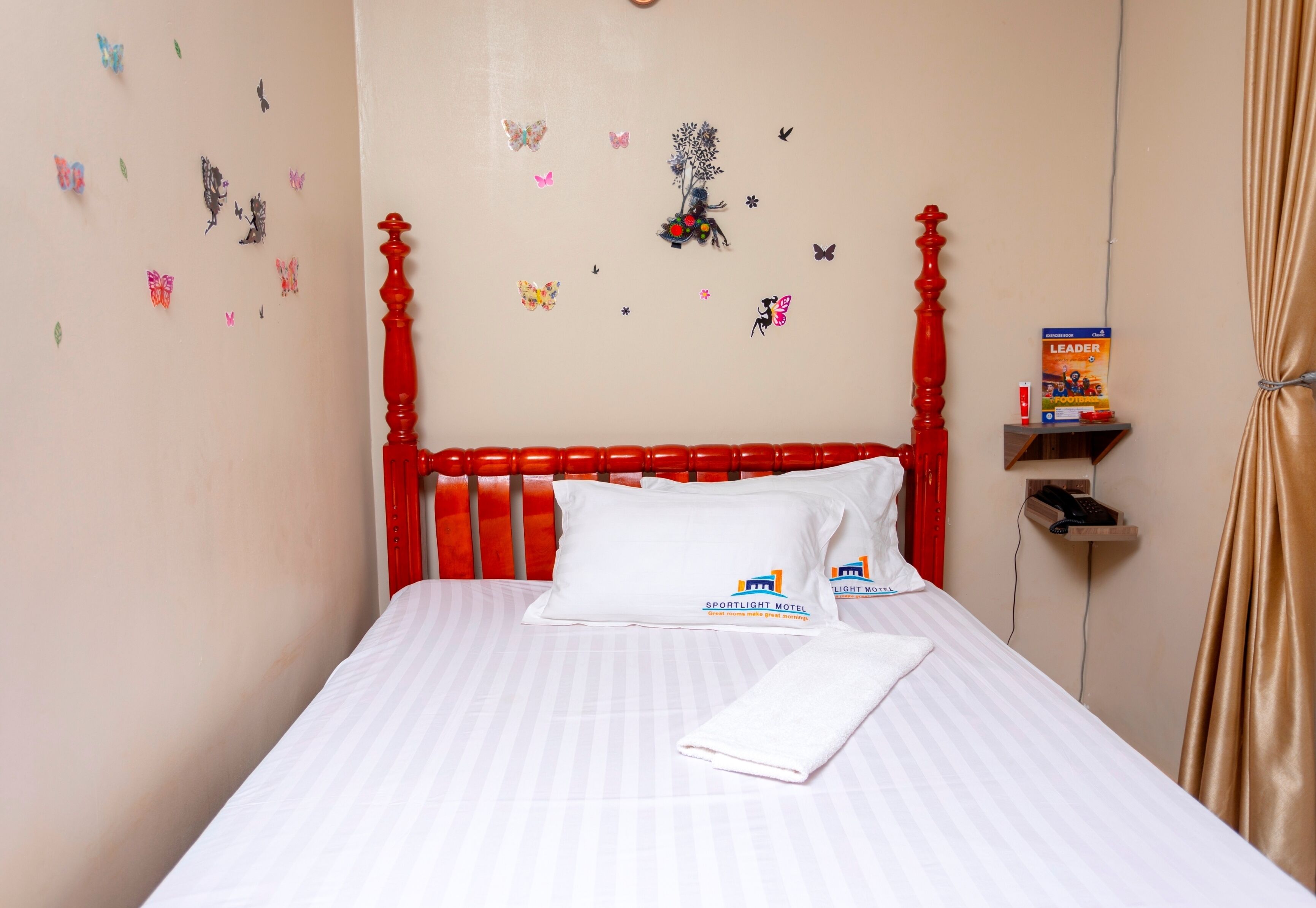 A neatly made bed with white bedding, a red headboard, and decorative butterfly wall stickers.