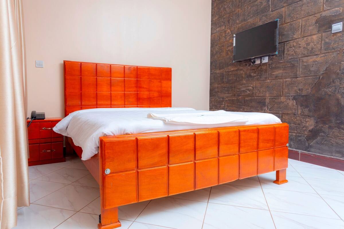 A room with a bed, a red nightstand, a wall-mounted TV, and a stone wall.