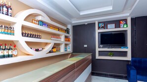 A bar area with shelves of liquor bottles, a wooden counter, a television, and framed certificates on the wall. - Spotlight Motel (Kampala)