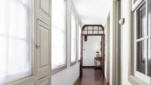 A hallway with white walls, wooden flooring, and large windows.