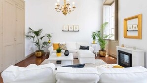 A modern living room with a white sofa set, a chandelier, and potted plants.