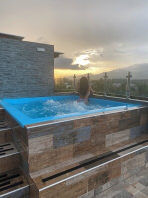 A person in a swimming pool with a view of a sunset and mountains in the background. - Apartment with jacuzzi (Santiago De Los Caballeros)