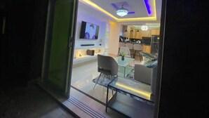 A modern interior with a glass door leading to a living area, a flat-screen TV, and a dining area with chairs and a table. - Apartment with jacuzzi (Santiago De Los Caballeros)