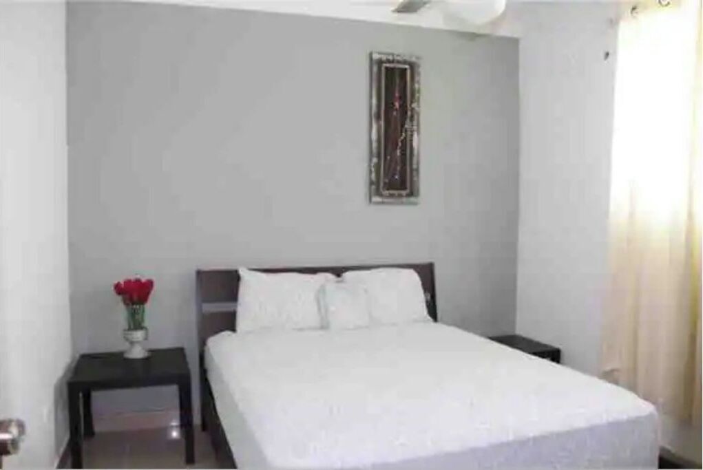 A neatly made bed in a hotel room with a small bedside table and a vase of flowers.