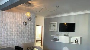Een moderne woonkamer met een bank, een eettafel, een aan de muur bevestigde televisie en decoratieve objecten.