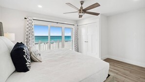 A bedroom with a bed, a ceiling fan, a view of the ocean, and a white door.