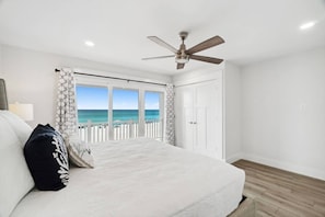 A bedroom with a bed, a ceiling fan, a view of the ocean, and a white door.