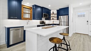 A modern kitchen with dark blue cabinets, stainless steel appliances, and a white countertop.