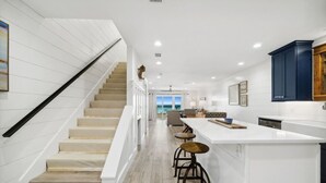 A modern kitchen with a central island, bar stools, and a staircase.