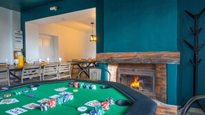 Una mesa de billar con fichas de póker y cartas, una chimenea y un comedor con sillas y mesas.
