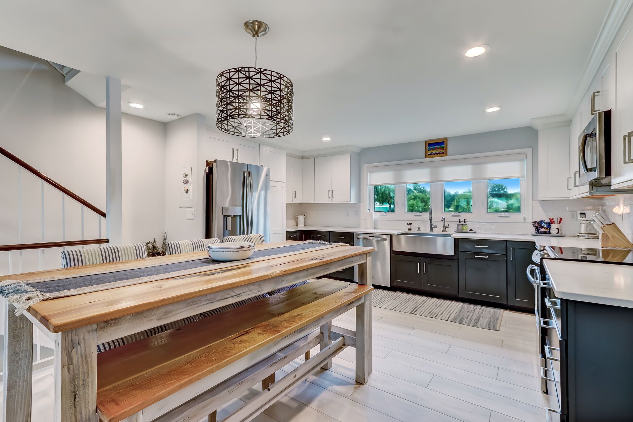 Una cocina moderna con armarios blancos, un refrigerador de acero inoxidable y un ventanal con vistas a árboles.