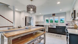A modern kitchen with white cabinets, a stainless steel refrigerator, and a large window with a view of trees. - Amelia Island Oceanfront 3 Bedroom - Sandpiper Villa (Fernandina Beach)