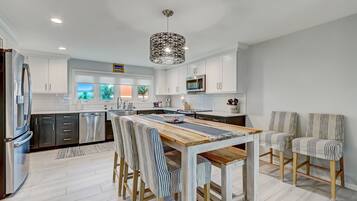 Una cocina moderna con armarios blancos, electrodomésticos de acero inoxidable y una mesa de comedor de madera con sillas a rayas.
