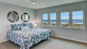 A bedroom with a bed, two wall mirrors, a ceiling fan, and a view of the beach through large windows. - Amelia Island Oceanfront 3 Bedroom - Sandpiper Villa (Fernandina Beach)