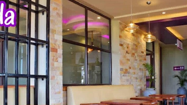 L’intérieur d’un restaurant avec des tables et des chaises en bois, un mur en briques et de grandes fenêtres.