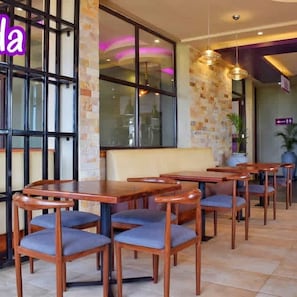 A restaurant interior with wooden tables and chairs, a brick wall, and large windows. - Tenda Suites and Restaurant (Entebbe)