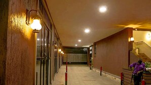 Un couloir d’hôtel avec un mur en bois, une personne debout près du comptoir d’accueil et un escalier.