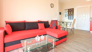A red sofa with black cushions, a glass coffee table with decorative items, and a dining area with a glass table and chairs. - Eros Sea View in Kentroma (Corfu)